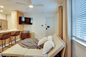 A modern hotel room with a bed, a desk, a chair, a TV, and a window with blinds. - 5 Mi to UF! Luxury 2-unit Combo w/ Hot Tub (Gainesville)