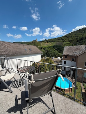 Un balcon avec une chaise et une table, donnant sur une piscine et un château situé sur une colline.