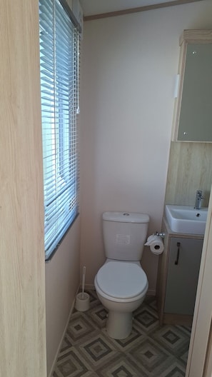 Ein kleines Badezimmer mit Toilette, Waschbecken und Fenster mit Jalousien.