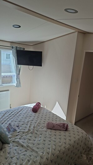 Ein Hotelzimmer mit einem Bett, einem flachbildfernseher an der Wand, einem Fenster mit Vorhängen und einer Heizung.