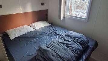 Ein Einzelbett mit Kopfteil, ein Fenster mit Vorhängen und ein Regal über dem Bett.