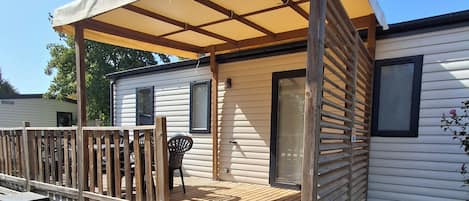 A mobile home with a wooden deck, a covered patio, and a grill.