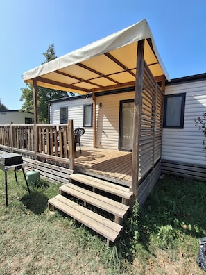 Une maison mobile dotée d’une terrasse en bois, d’un patio couvert et d’un barbecue.