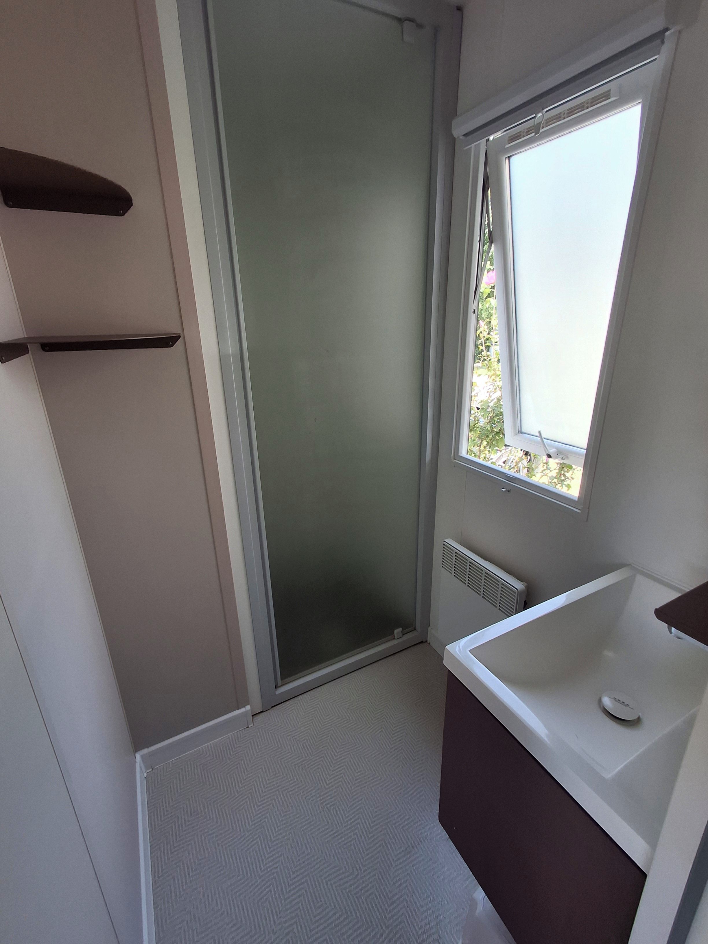 A small bathroom with a shower, a window, and a white sink.