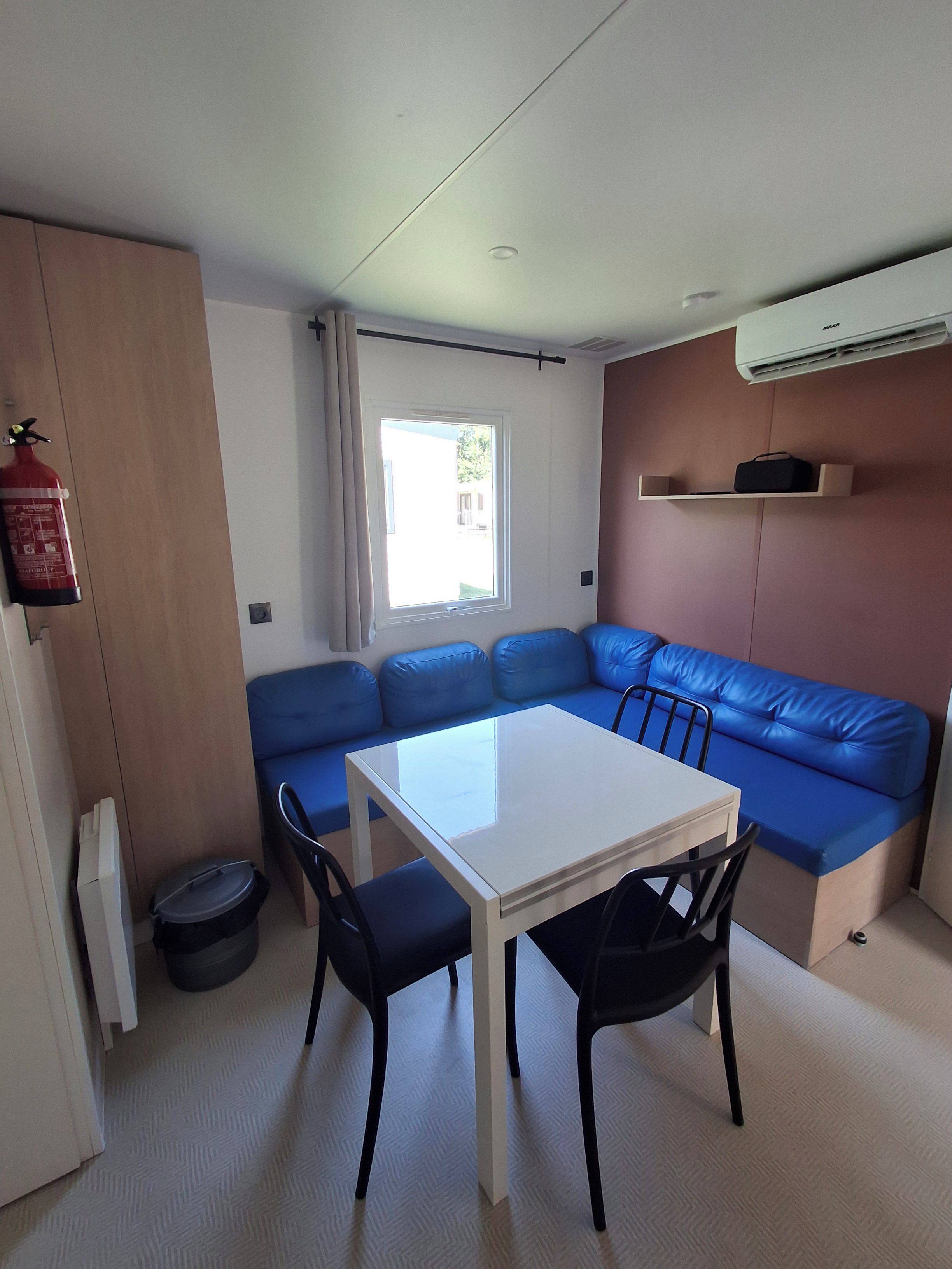 Un espacio habitable compacto con kitchenette, un sofá azul, una mesita y un ventanal.