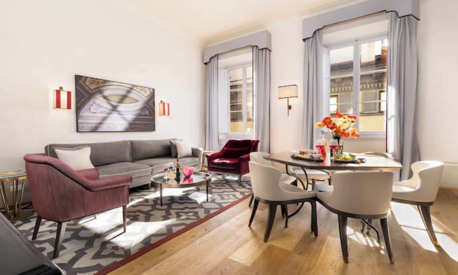 A modern living room with a grey sofa, red armchair, and a dining area with a table and chairs.