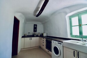 A compact kitchen with a washing machine, a coffee maker, and a window with a green frame. - Ambrosia Cave Villa with Seaview & Private Pool (Exo Gonia)