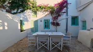A white outdoor patio with a table and chairs, surrounded by white walls and green shutters. - Ambrosia Cave Villa with Seaview & Private Pool (Exo Gonia)