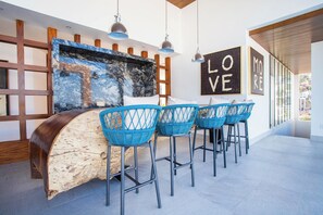 Un área de bar moderna con mostrador de mármol, sillas de mimbre azul, iluminación colgante y obras de arte en las paredes.