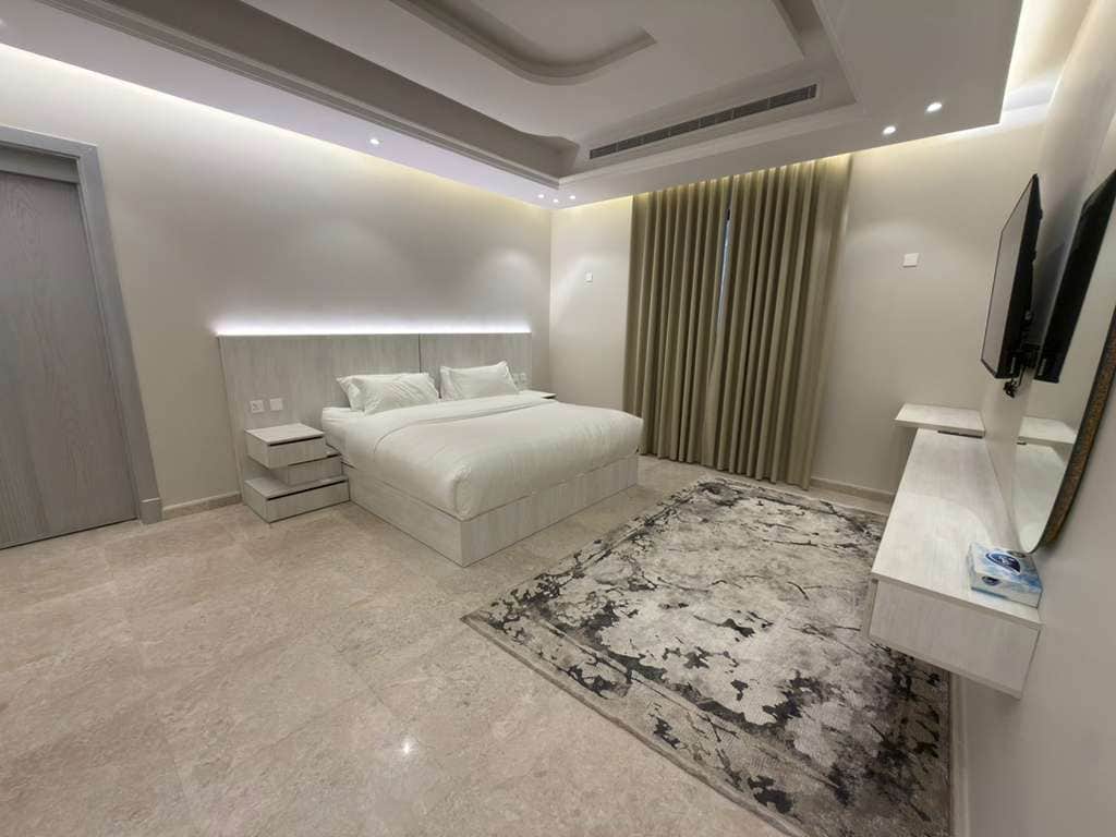 Un dormitorio moderno con una cama grande, mesitas de noche, un tocador con espejo y una alfombra estampada.