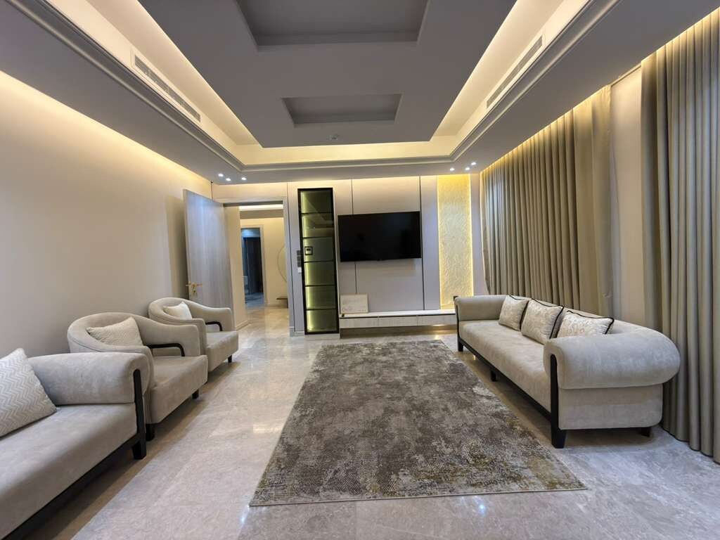Una sala de estar moderna con un televisor de pantalla plana, dos sofás, un tapete y un ventanal con cortinas.