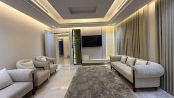 Una sala de estar moderna con un televisor de pantalla plana, dos sofás, un tapete y un ventanal con cortinas.