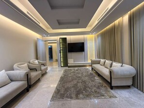 Una sala de estar moderna con un televisor de pantalla plana, dos sofás, un tapete y un ventanal con cortinas.
