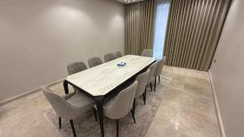 Un salón de conferencias con una mesa de mármol y seis sillas, un ventanal con cortinas y una lámpara empotrada en el techo.