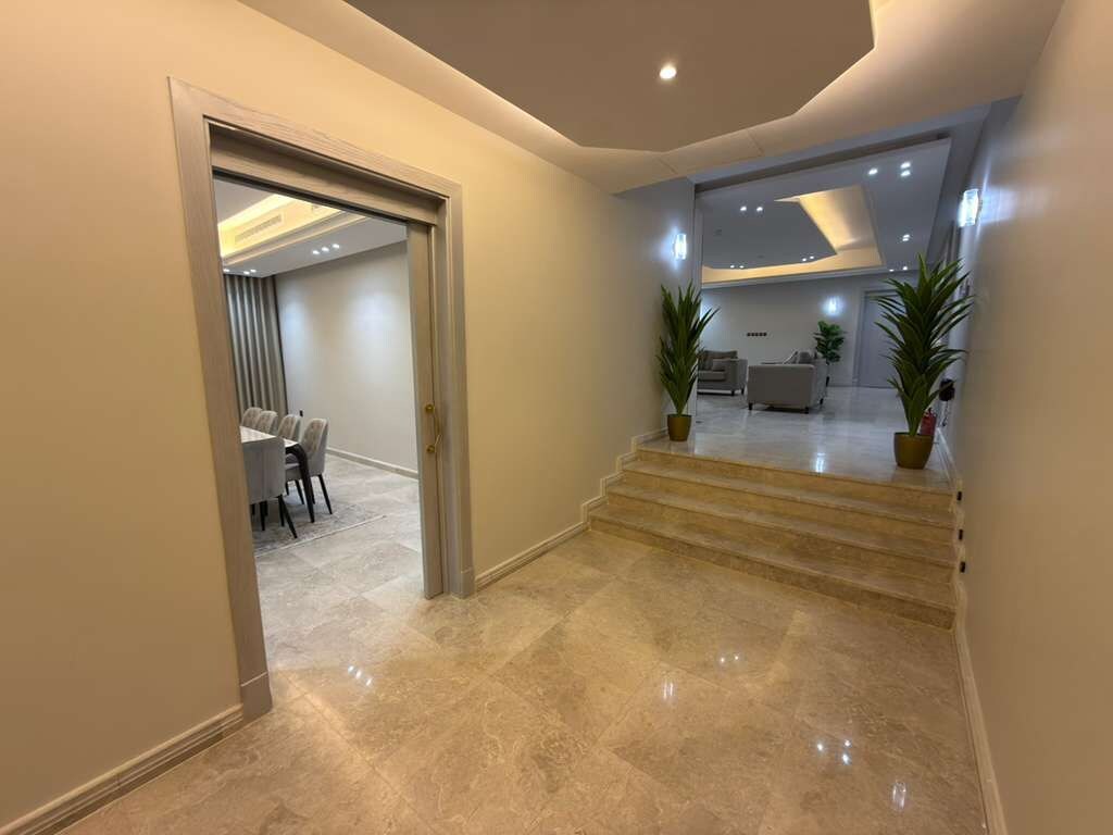 Un interior moderno con una escalera de mármol que conduce a una sala de estar con sofás y una mesa de comedor.