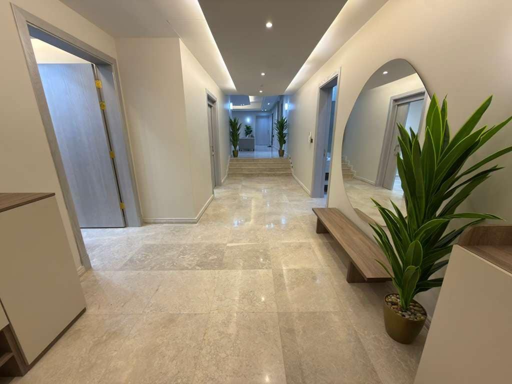 A hallway with a marble floor, a bench, and potted plants.