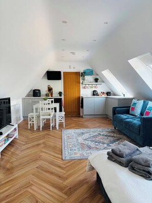 A compact living space with a kitchenette, a dining area, and a seating area with a sofa and a TV. - ‘The Loft’ Near Whitstable, Parking, EV, Courtyard (Yorkletts)