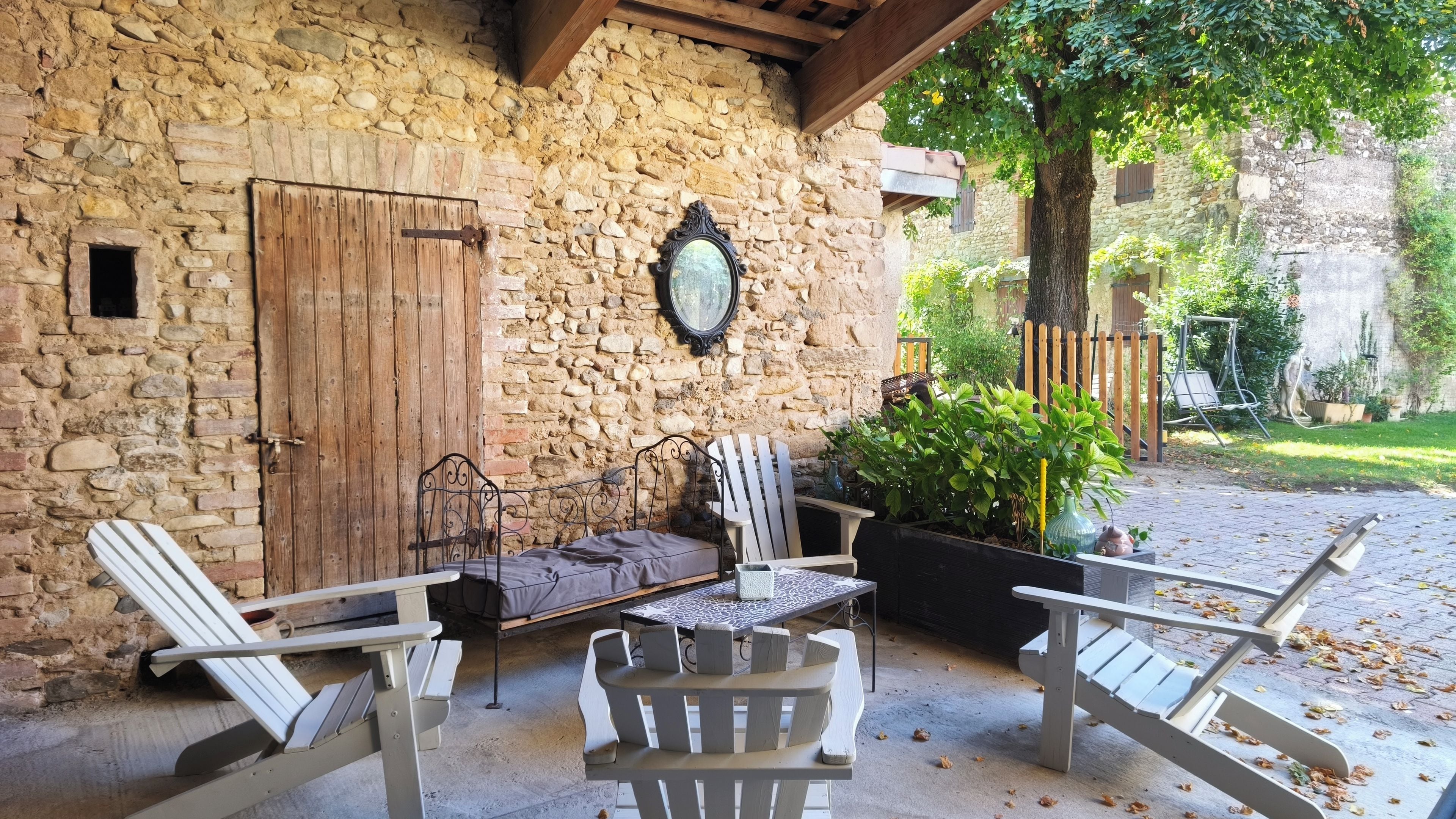 An outdoor seating area with Adirondack chairs, a table, and a stone wall backdrop.