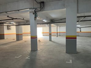 Eine überdachte Parkgarage mit Betonpfeilern, Deckenbeleuchtung und einer sichtbaren Klimaanlage an der Wand.
