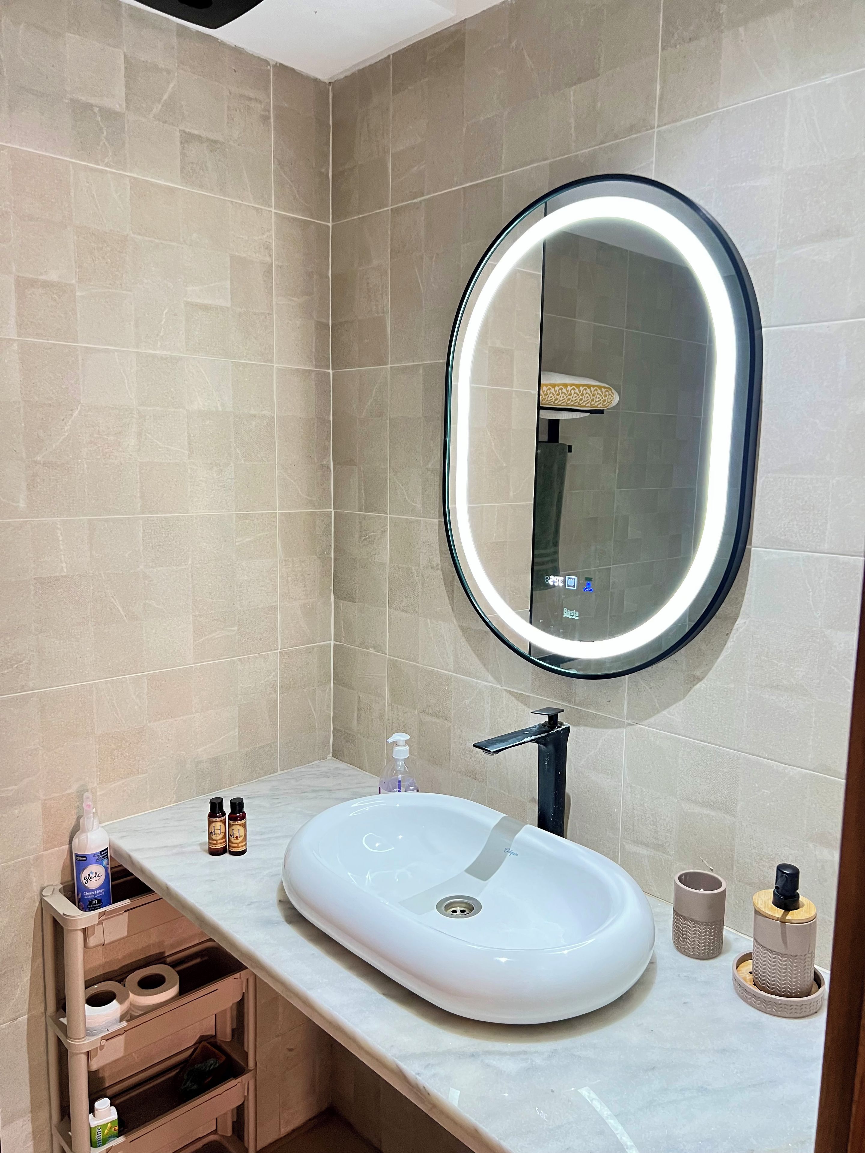 A bathroom with a white sink, a round mirror with a light, and a shelf with toiletries.