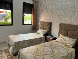 Ein Hotelzimmer mit zwei Betten, einem Fenster mit Jalousien, einer Wand mit Muster und einem kleinen Nachttisch.