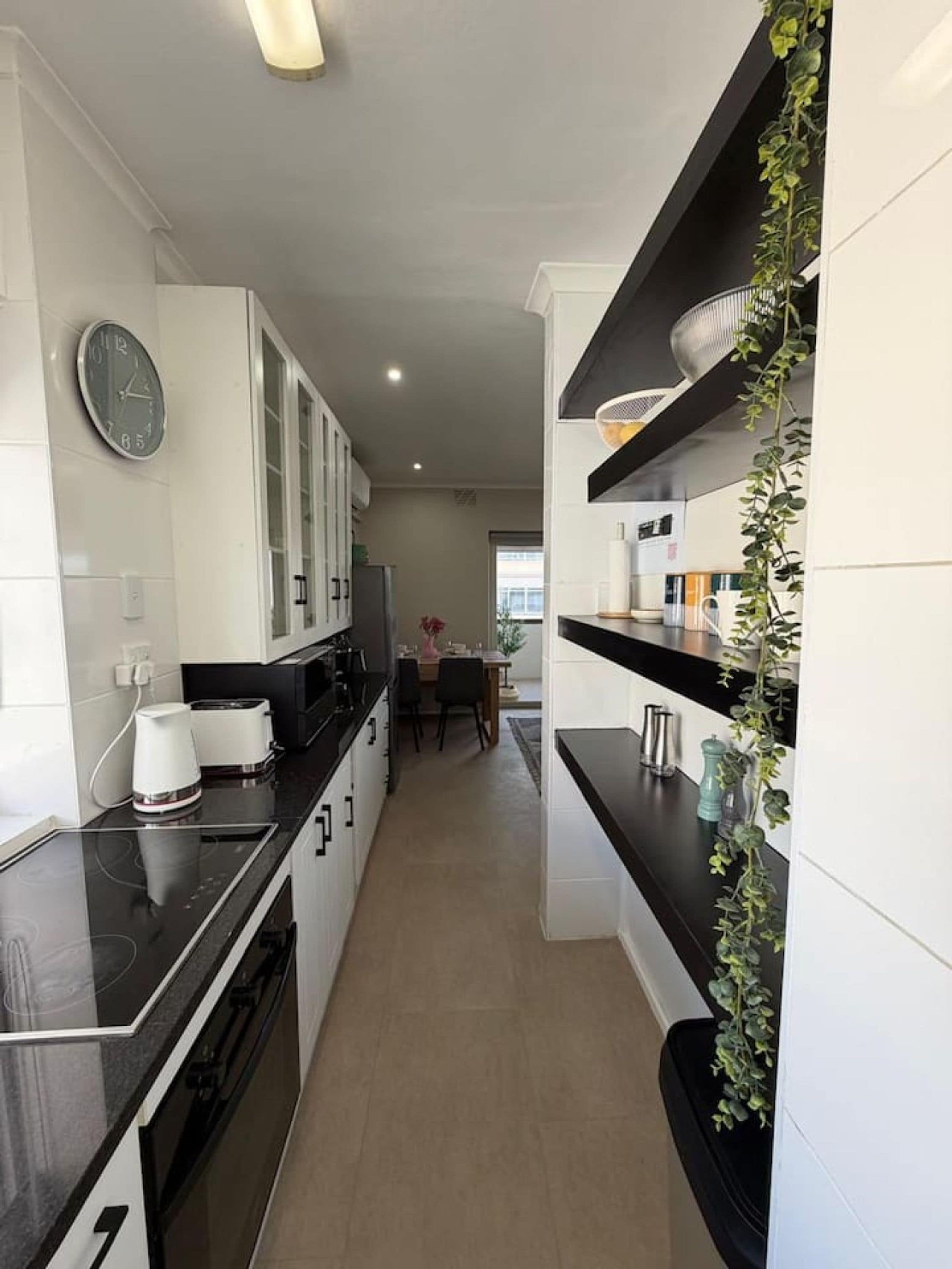 Une cuisine moderne avec des meubles blancs, un plan de travail noir et une horloge au mur.