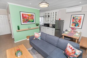 Un salon moderne avec un canapé gris, une table basse en bois et un coin repas avec une table dressée pour deux personnes.