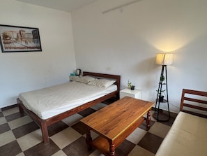A single bed with a wooden frame, a bedside table with a lamp, and a checkered floor. - Doon Arvaya (Dehradun)