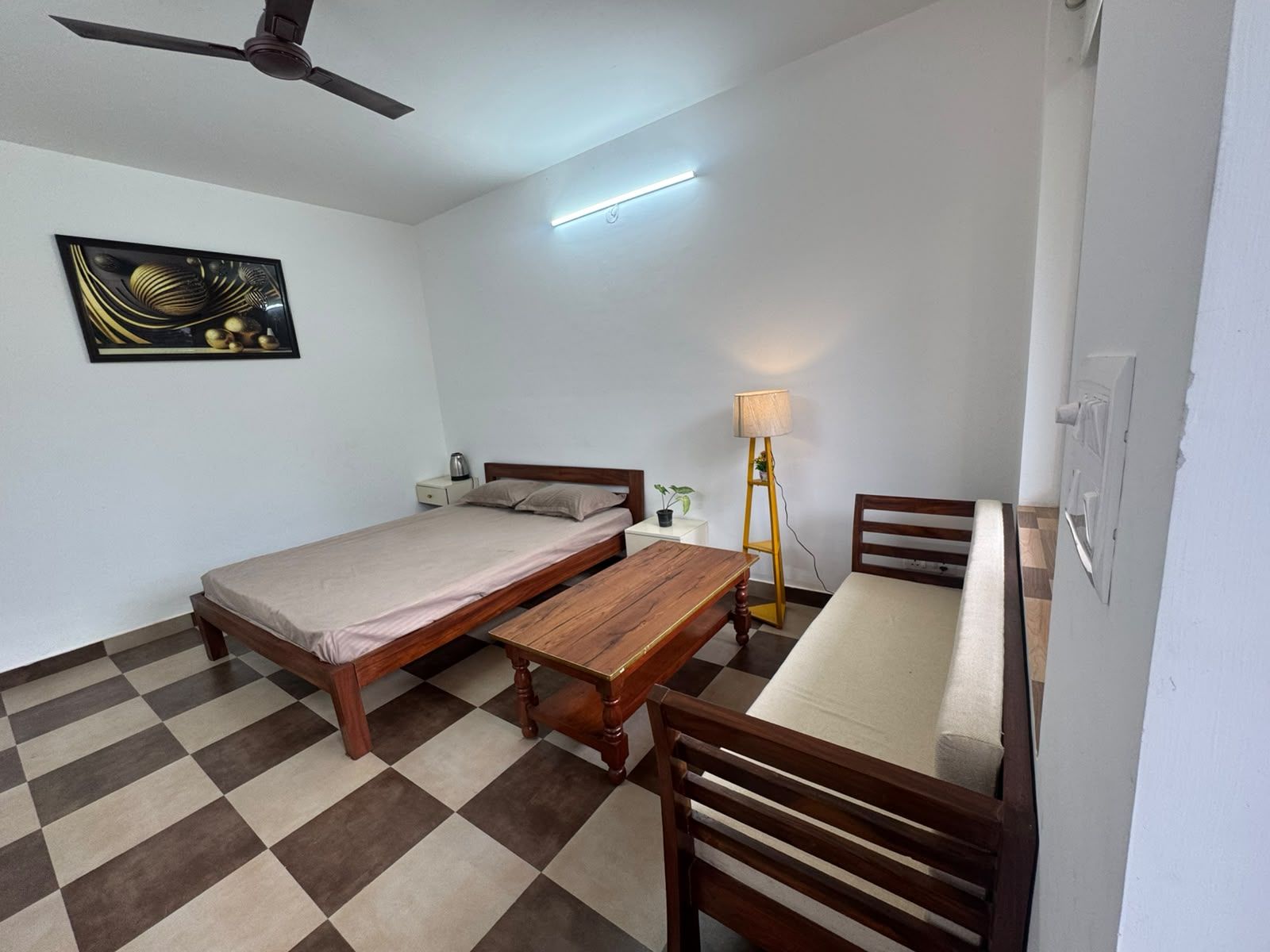 A room with a bed, a table, a chair, a floor lamp, and a ceiling fan.