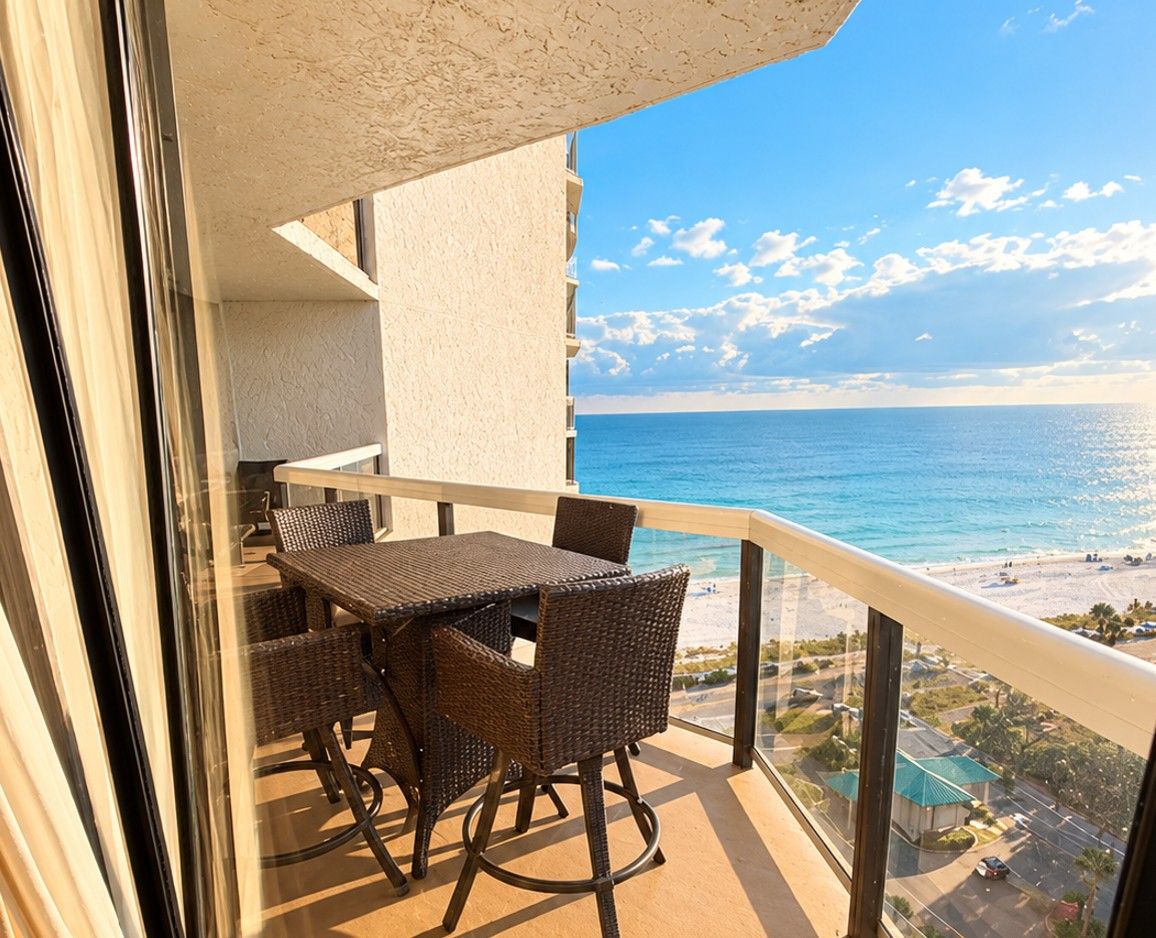 Ein Balkon mit Tisch und Stühlen mit Blick auf einen Strand und den Ozean.