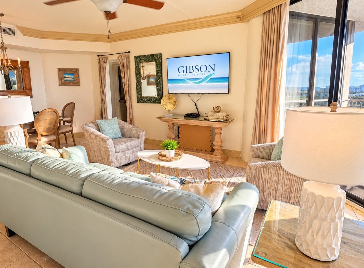 Ein Wohnzimmer mit einer Couch, Sesseln, einem Couchtisch und einem Fernseher, der 'Gibson Beach Rentals' anzeigt.