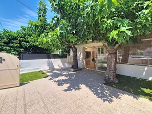 A covered outdoor area with a paved floor, surrounded by trees and a white wall. - Fully renovated vacation home, an 8-minute walk from the ocean (Vendres)