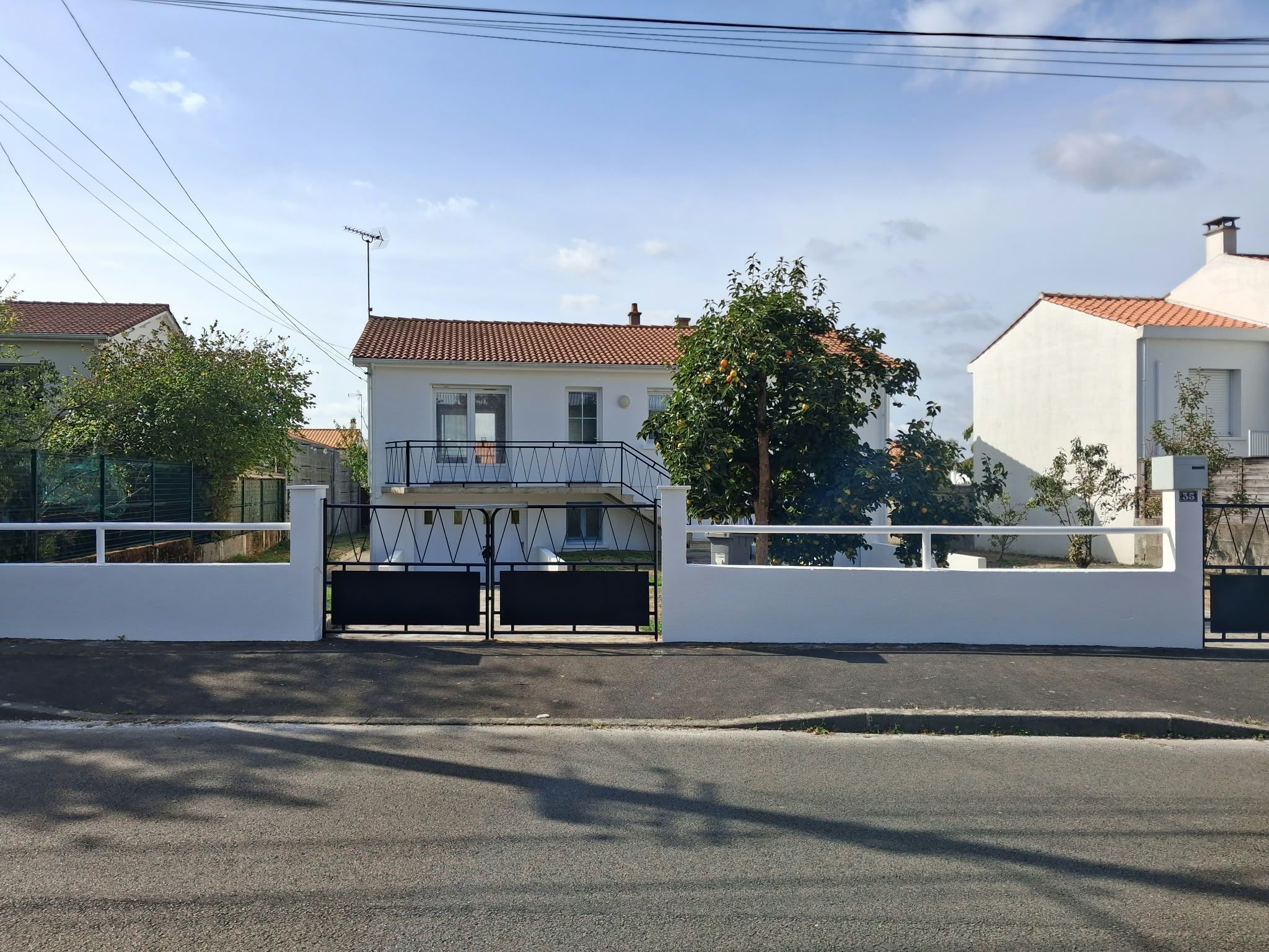 A gated residential area with a white building, a red-tiled roof, and a clear sky.