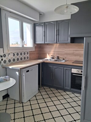 A kitchen with grey cabinets, a wooden countertop, a built-in dishwasher, and a black and white checkered floor.