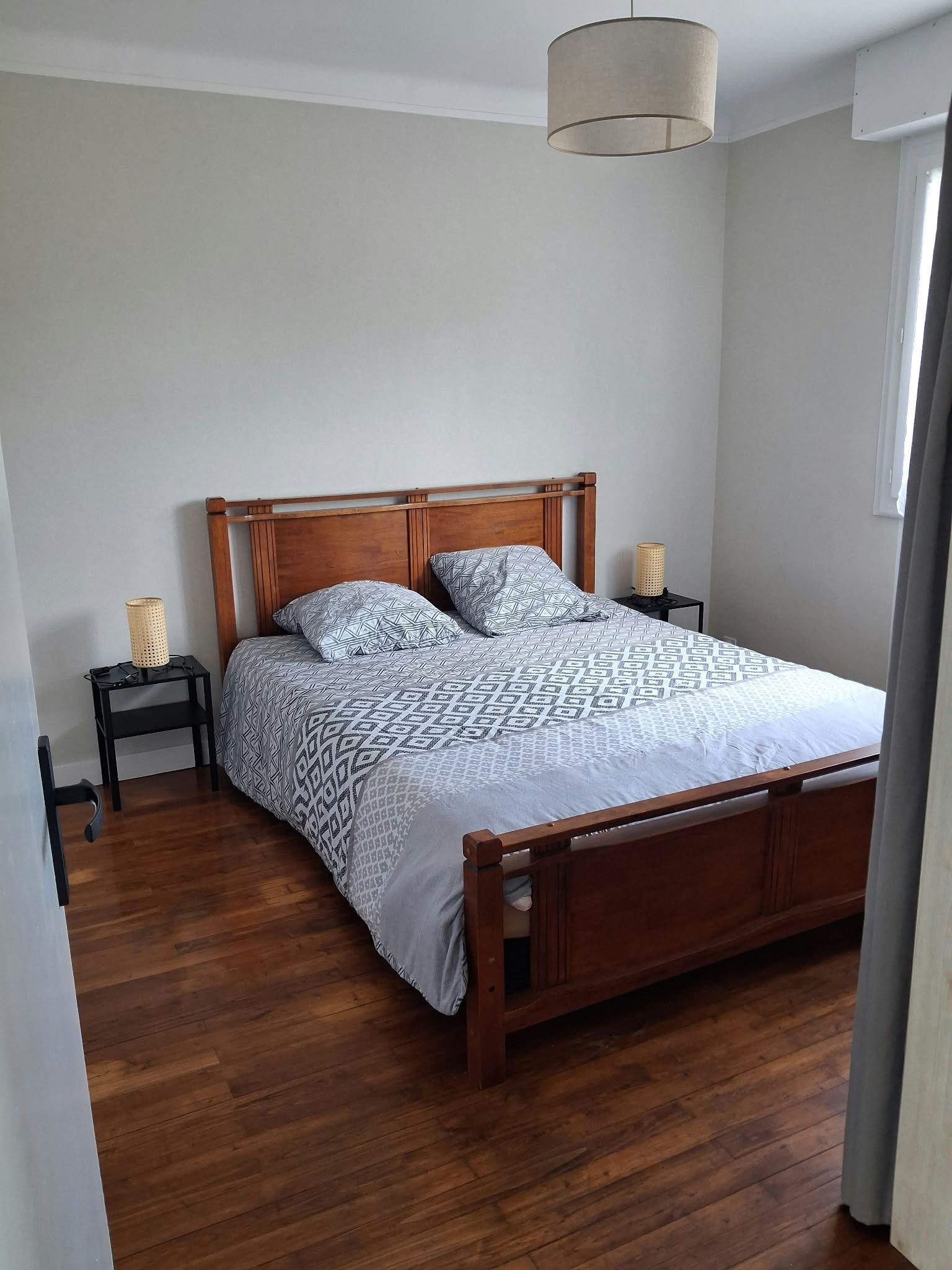 Une chambre à coucher avec un lit en bois, une literie à motifs, une lampe de chevet et un luminaire suspendu.