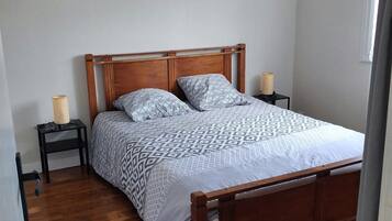 Een slaapkamer met een houten bed, beddengoed met een patroon, een bedlampje en een hangende lamp.