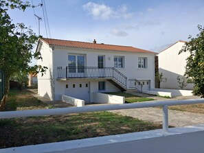 A two-story house with a balcony, a small front yard, and a paved driveway.