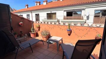 Un patio exterior con dos sillones, una mesita y plantas en macetas.