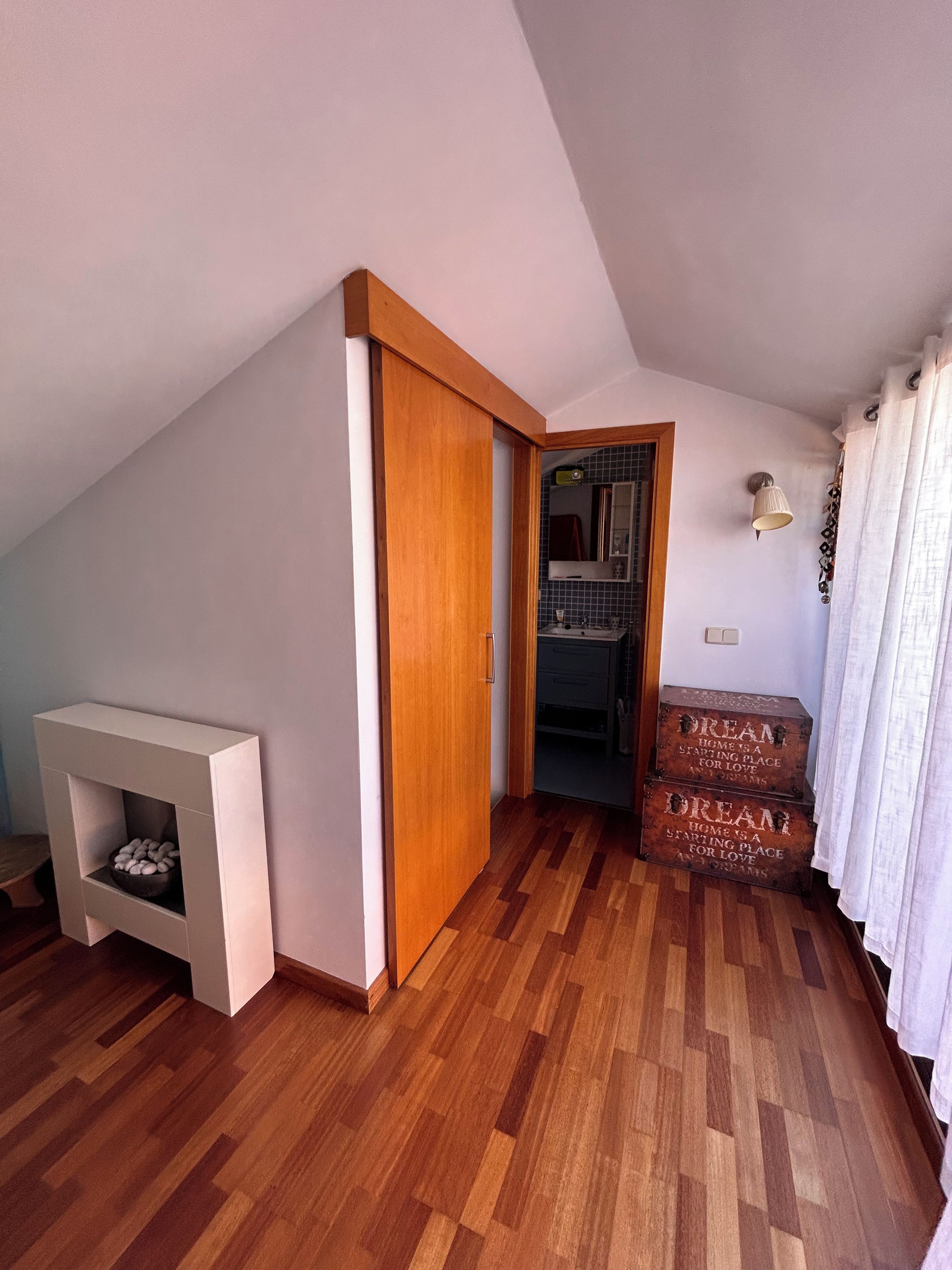 Una habitación con piso de madera, una chimenea blanca, una puerta de madera y un conjunto de cofres de madera con inscripciones.
