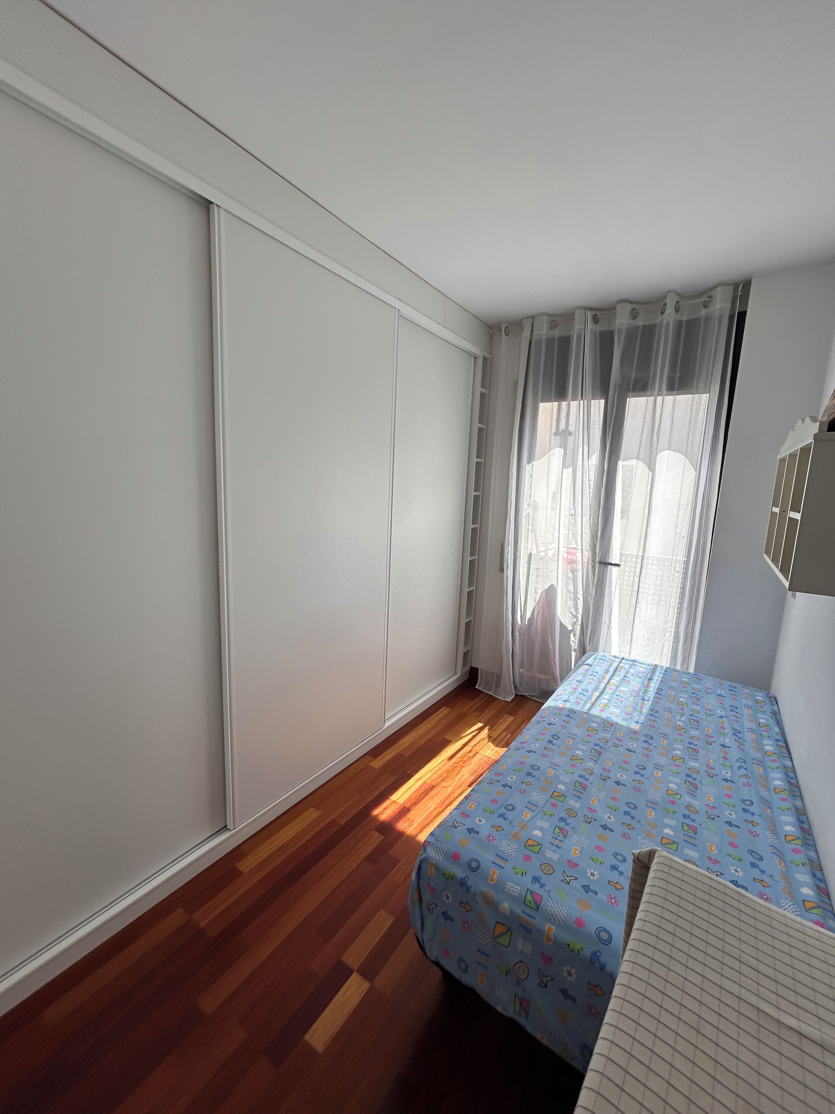 Un dormitorio con cama, armario y ventana con cortinas.