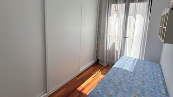 Un dormitorio con cama, armario y ventana con cortinas.