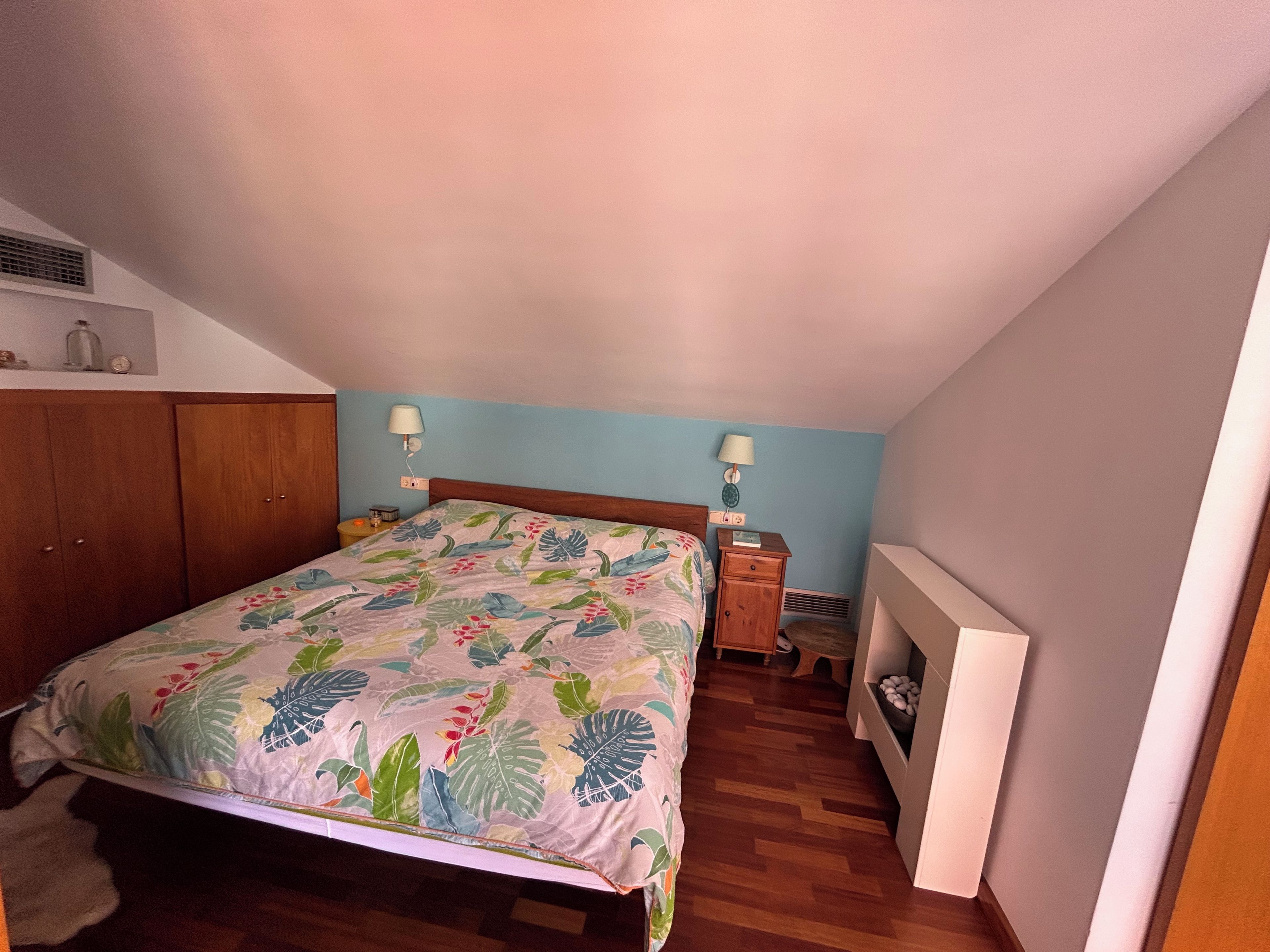 A bedroom with a bed, wooden wardrobe, nightstands, and a radiator.