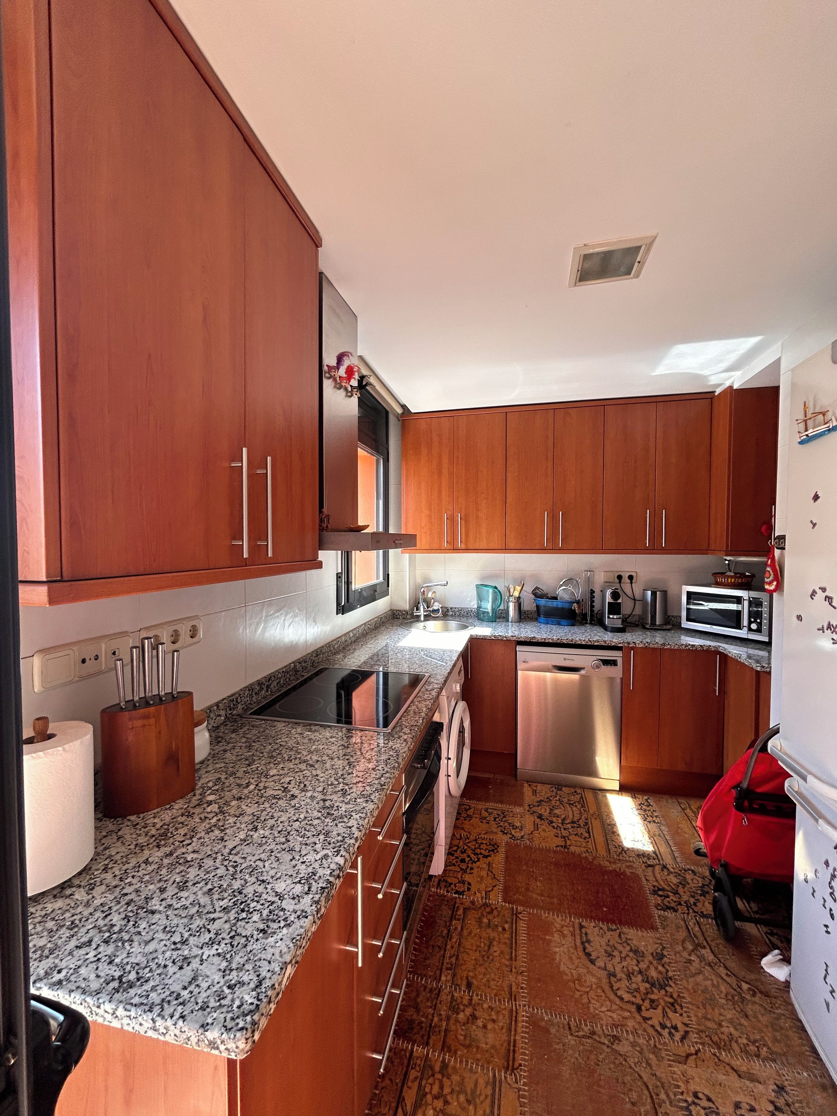A kitchen with wooden cabinets, a granite countertop, a dishwasher, and a red bag on the floor.