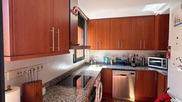 A kitchen with wooden cabinets, a granite countertop, a dishwasher, and a red bag on the floor.