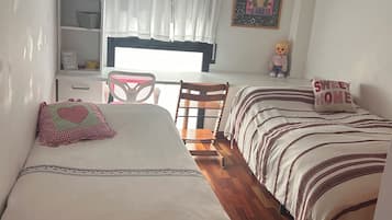Un dormitorio con dos camas, una estantería, un escritorio y una ventana con cortinas.