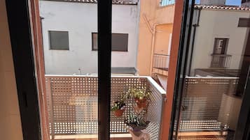 Een balkon met een metalen hekwerk, plantenbakken en vrij uitzicht op omliggende gebouwen.