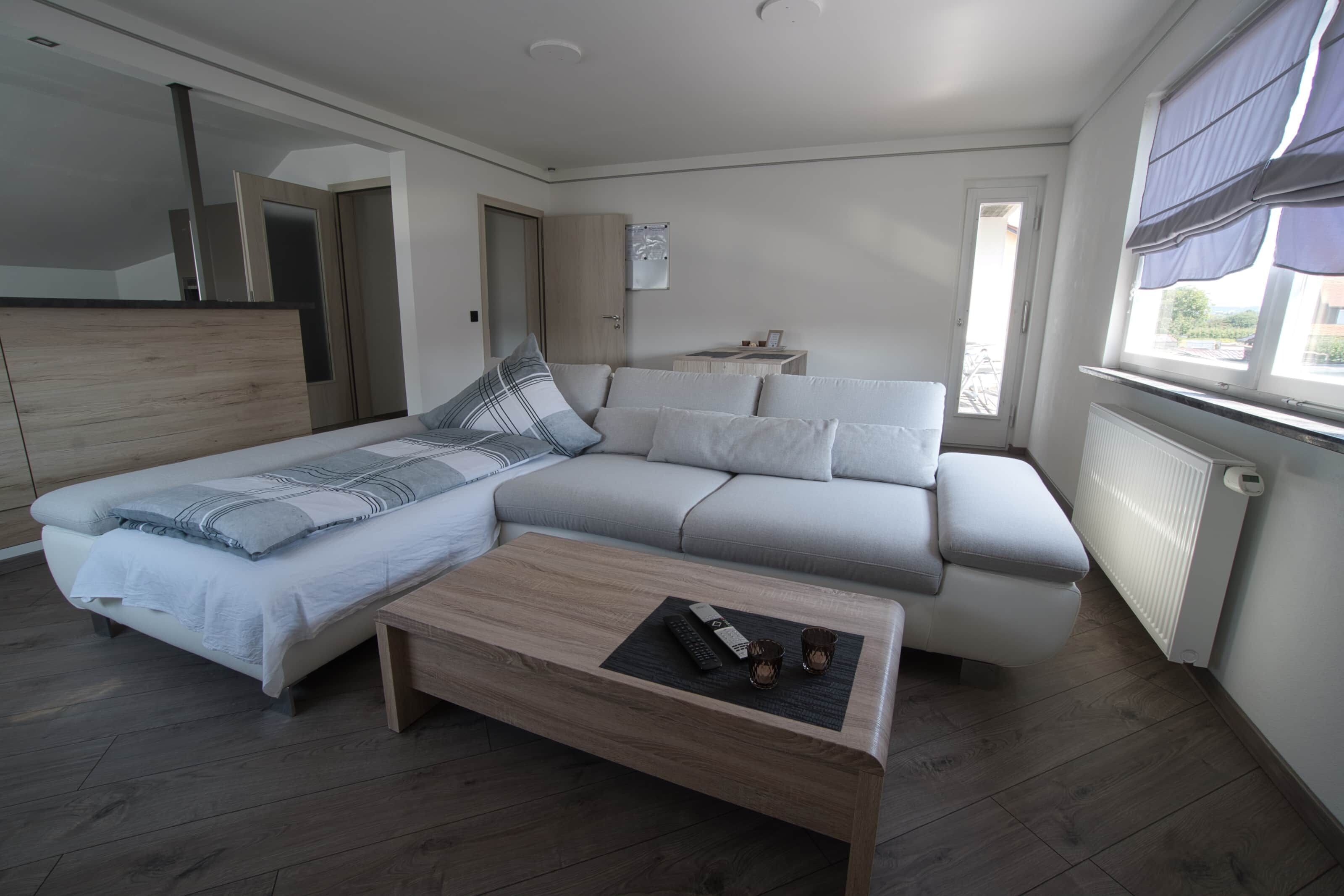 A modern bedroom with a bed, sofa, and a small table with remote controls and glasses.