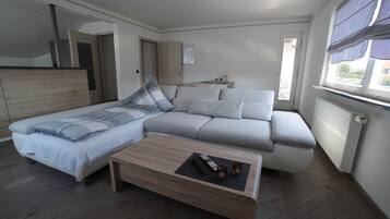 A modern bedroom with a bed, sofa, and a small table with remote controls and glasses.