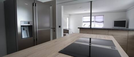 A modern kitchen with a built-in refrigerator, a wooden countertop, and a window with blinds.