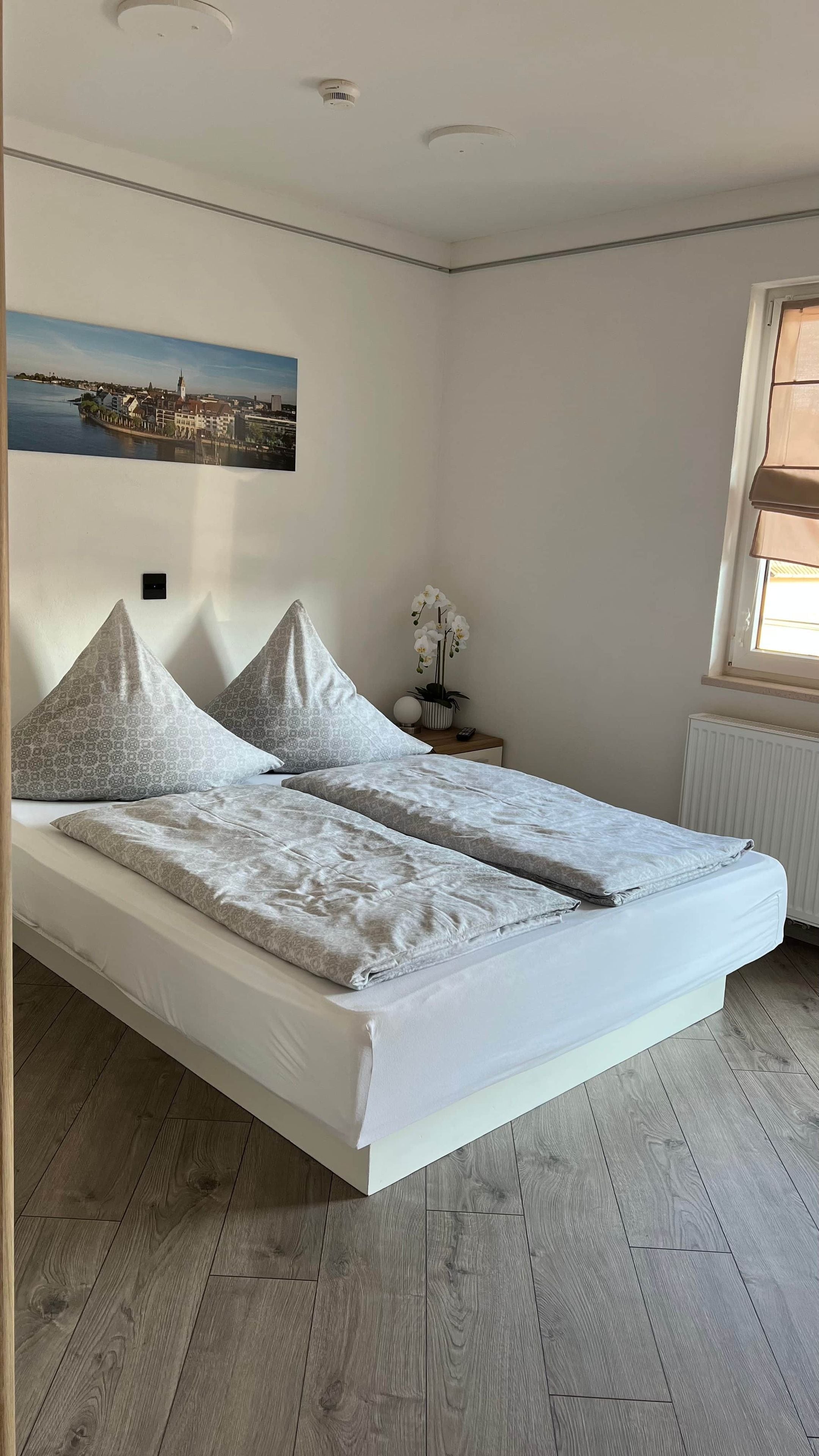 A bedroom with a bed, a nightstand, a window, and a wall-mounted picture.